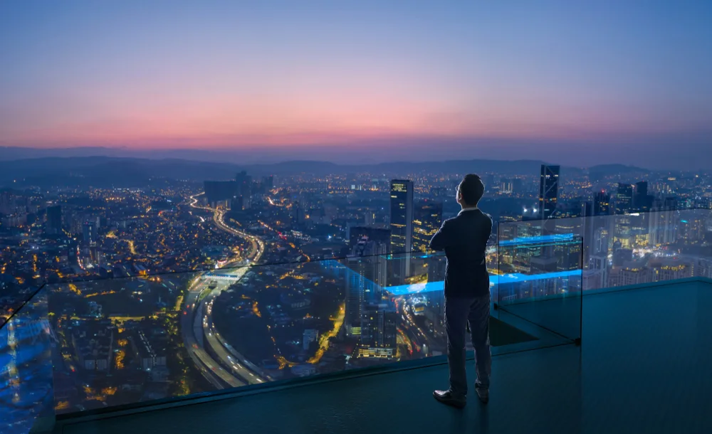 Businessman overlooking city skyline at night, symbolizing vision, ambition, and the future of mobile app development communities.