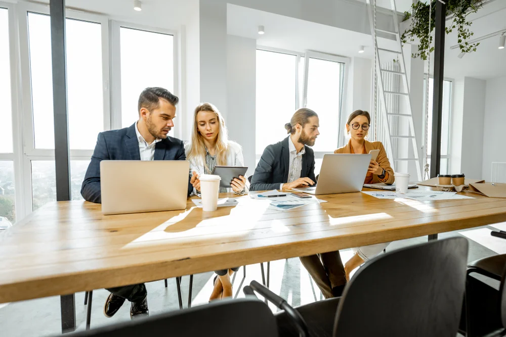 Young creative professionals collaborating at a large meeting table in a bright, modern office space.