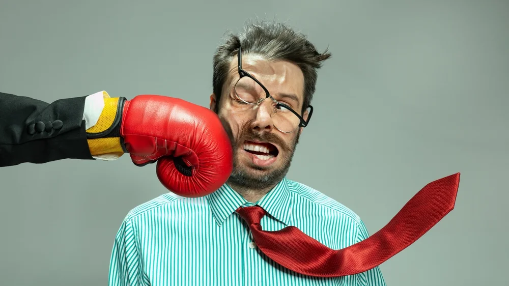 Businessman in red tie getting punched, symbolizing the risks of poor tech decisions in app development and business strategy.