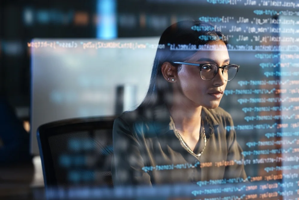 Female programmer coding at night with holographic data overlays, representing cross-platform app development and tech analysis.