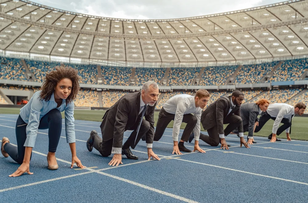 Business professionals lined up on a race track symbolizing competitive startup environment and the need for strong UX/UI design.