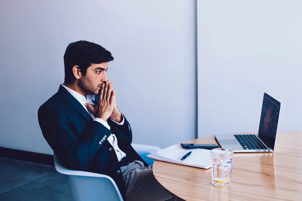 Worried office worker staring at laptop, stressed by delays and slow system performance.