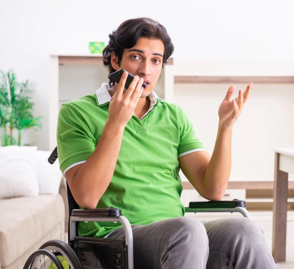 Young man in a wheelchair using a laptop at home, representing the importance of accessible digital design.