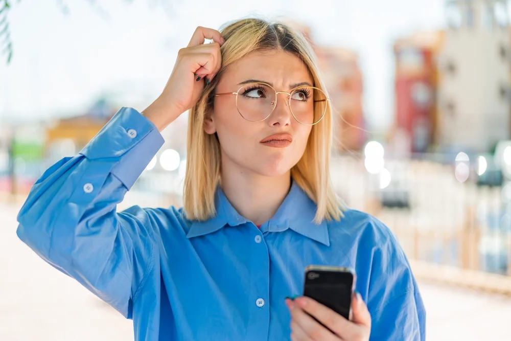 Confused young woman using a smartphone outdoors, unsure of how to proceed due to unclear app onboarding.
