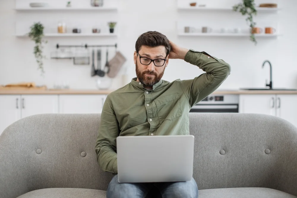 Confused man shrugging while using laptop, unsure of what action to take due to unclear call to action.